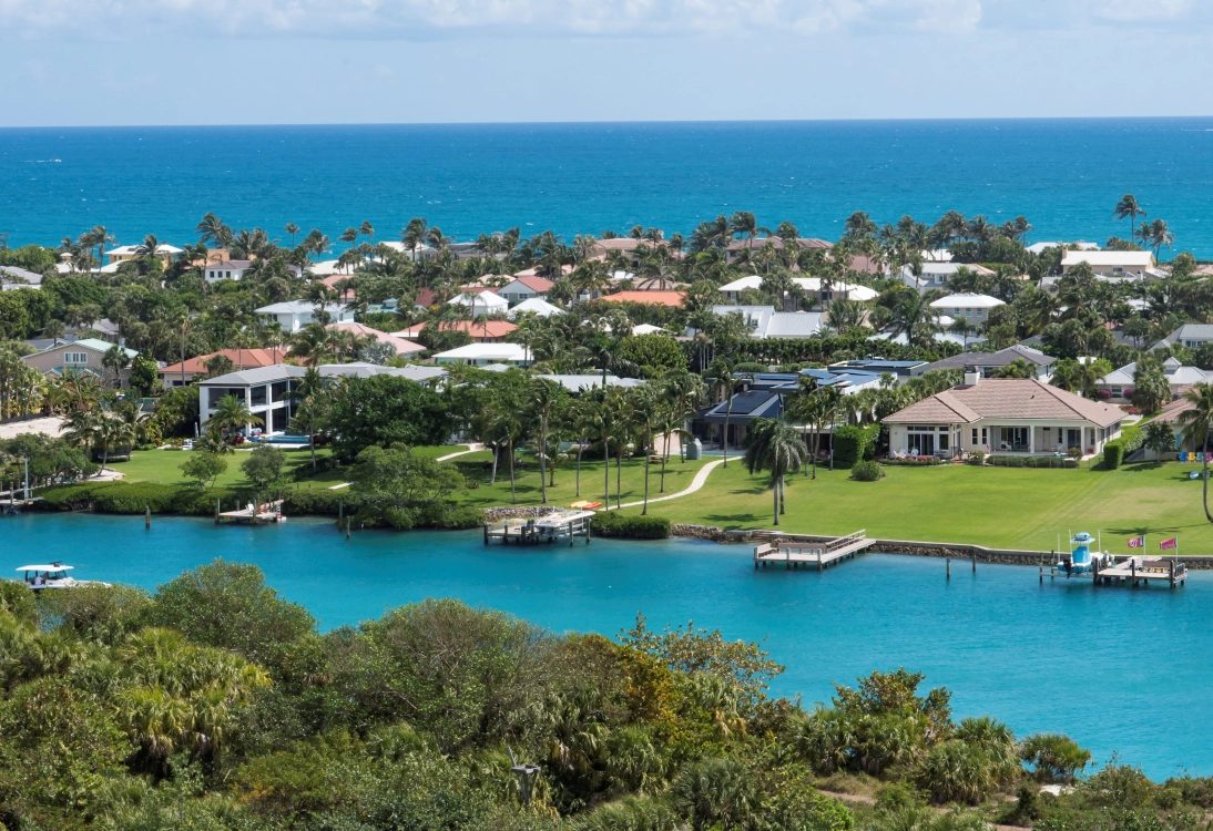 Waterfront homes and docks along the Jupiter Inlet, with the Atlantic Ocean behind them