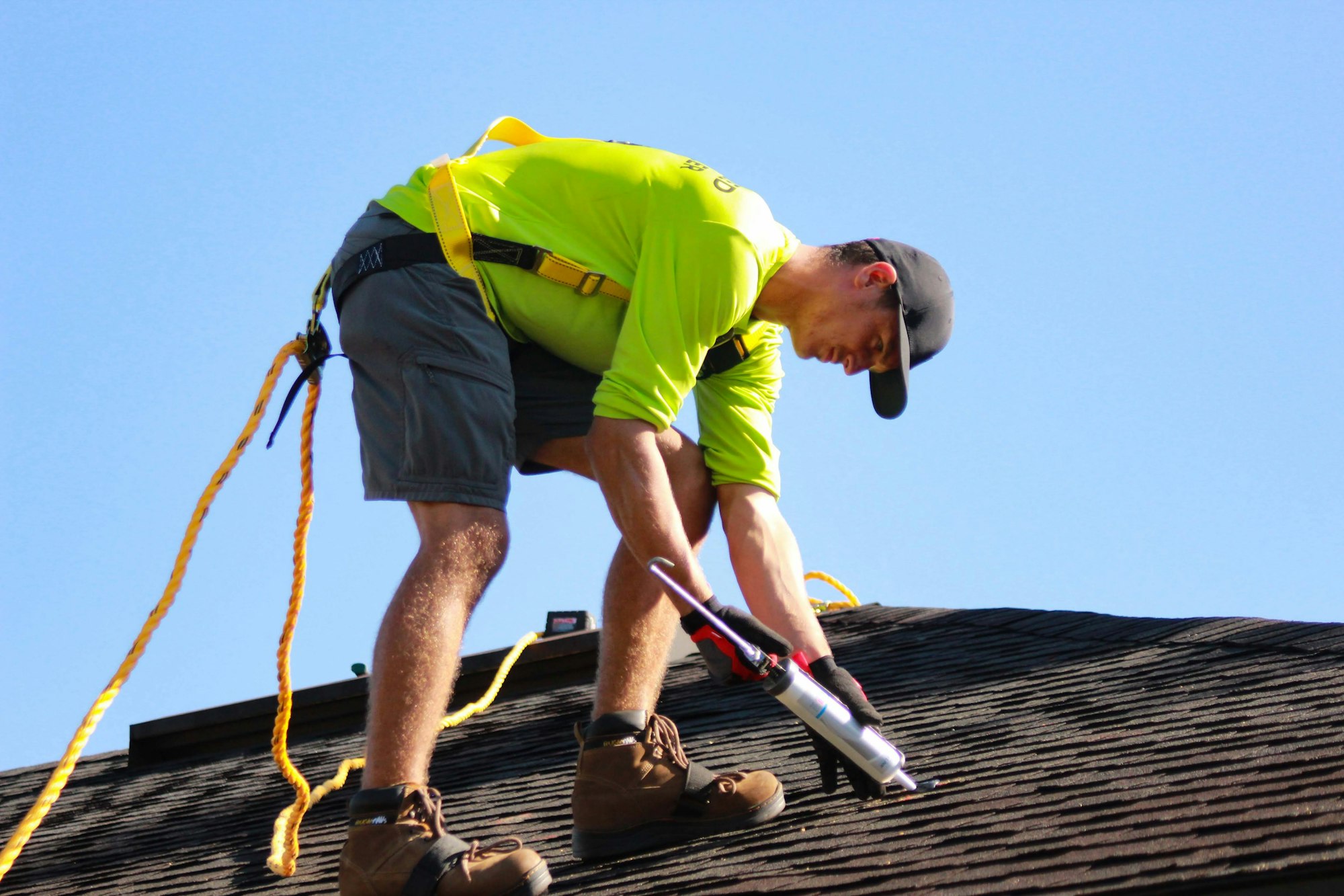 Roofer in a lime shirt working on a roof under a clear sky
